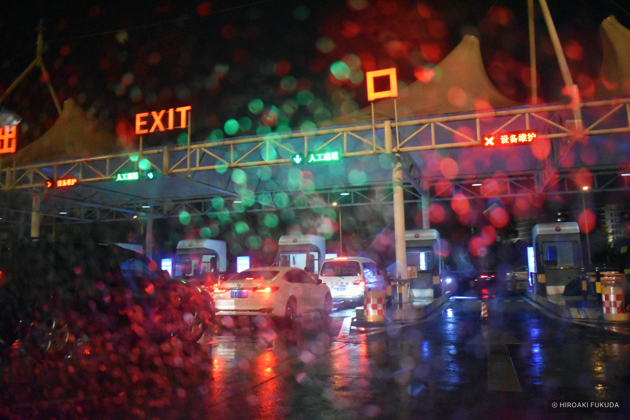 雨粒のついたガラス越しに、夜の車列と赤いテールランプが見える写真